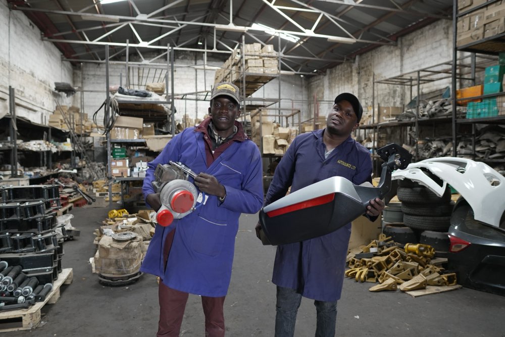 Ajale Enterprises staff holding a turbocharger and a truck body panel in the Nairobi warehouse